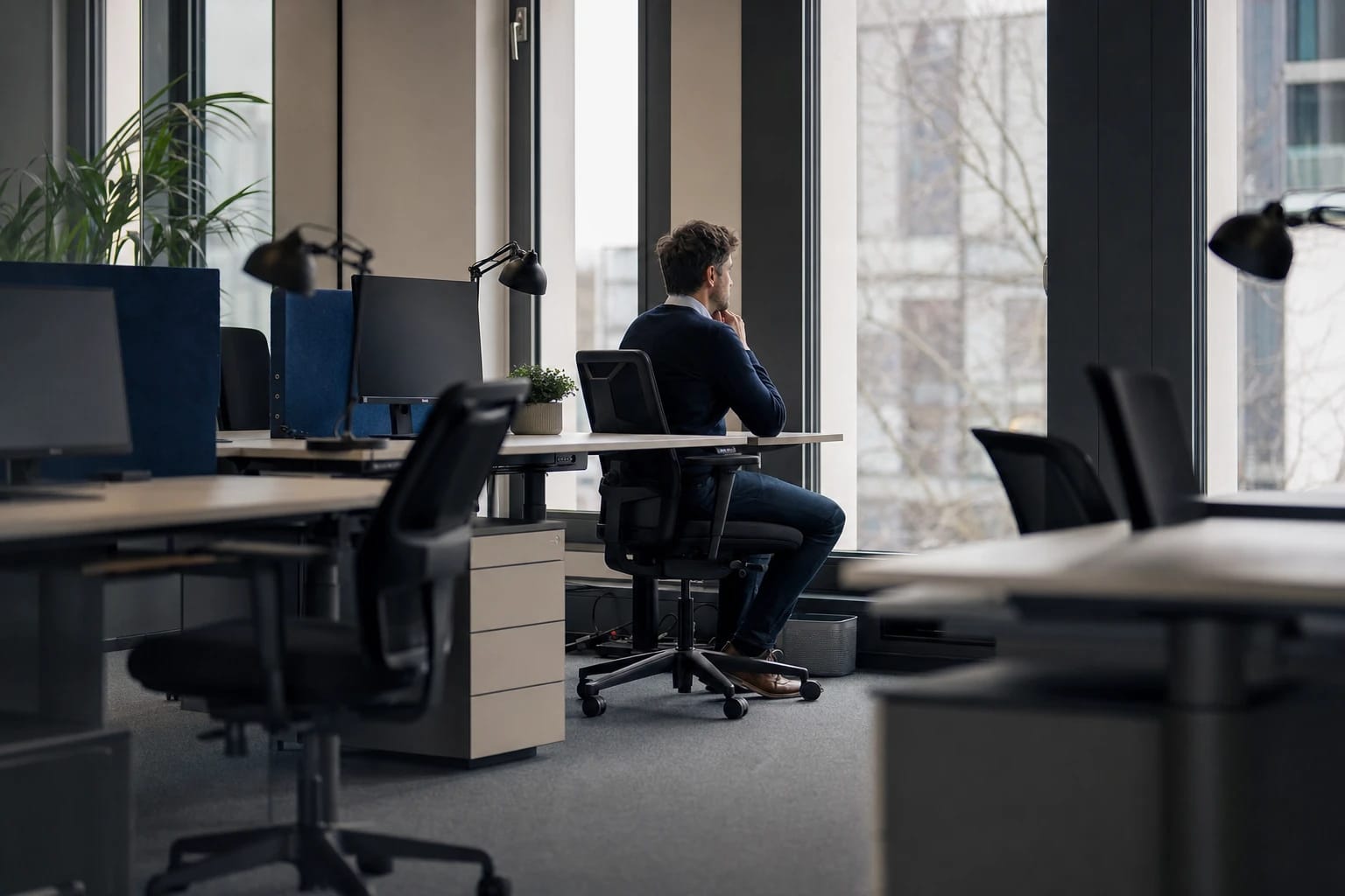 KI-generiertes Bild: Eine Person sitzt allein und niedergeschlagen am Arbeitsplatz, abseits der leeren Schreibtische der Kollegen.