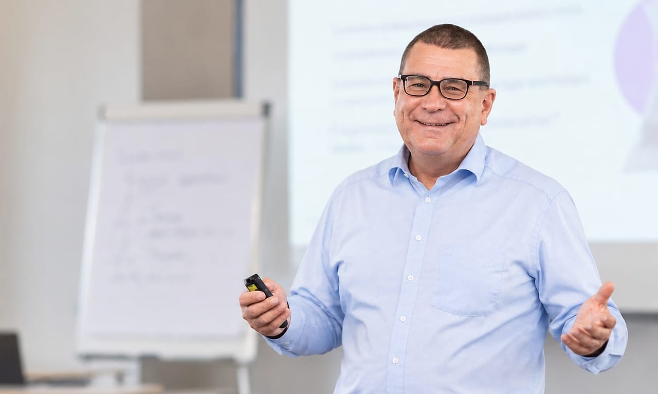 KI-generiertes Bild: Alexander Preidt mit Presenter vor einem Flipchart im Seminarraum