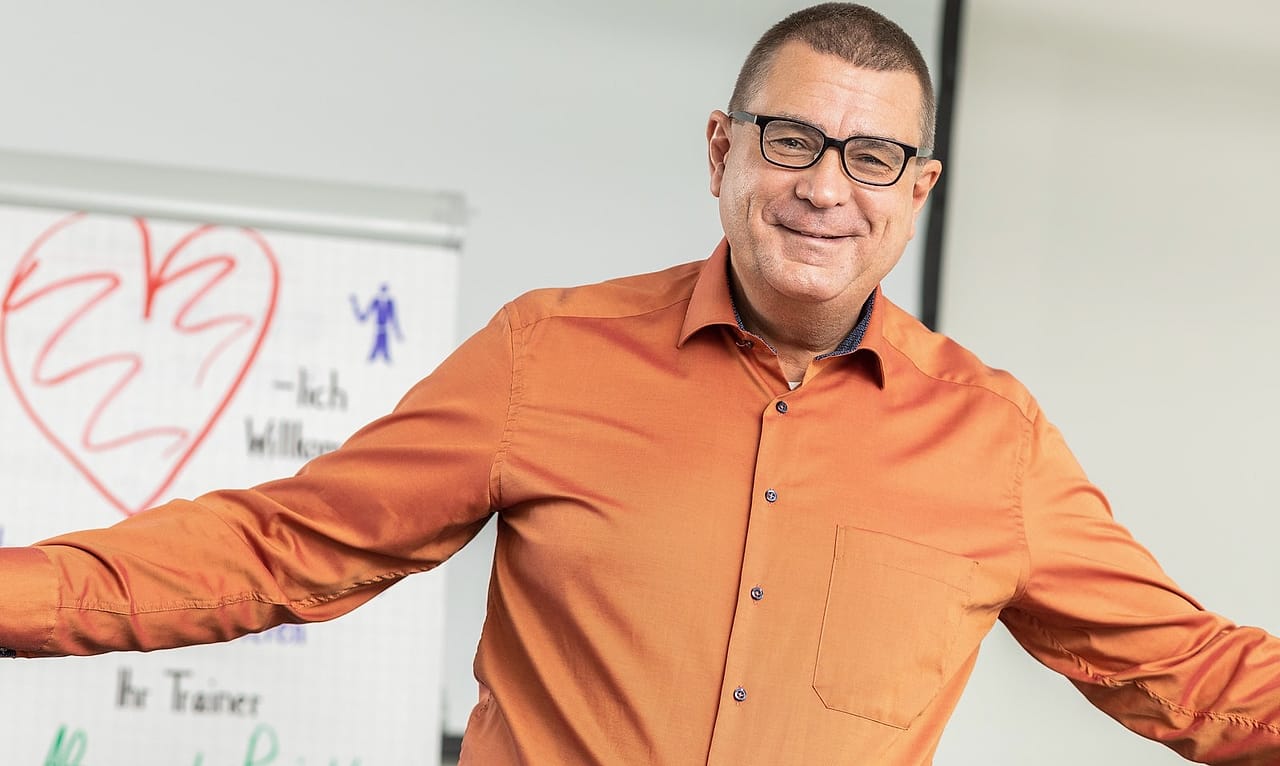 Alexander Preidt mit offenen Armen vor einem Flipchart im Seminarraum